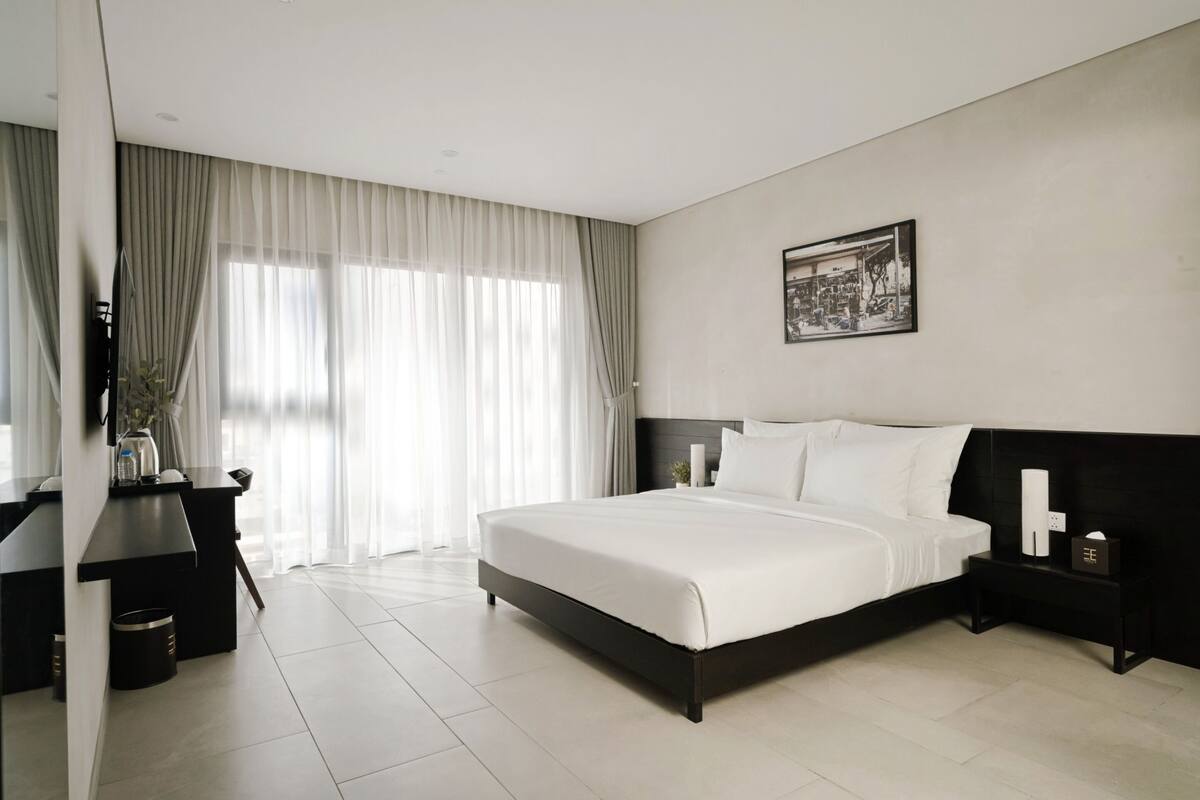 A modern hotel room with a large bed, a desk, and a nightstand.