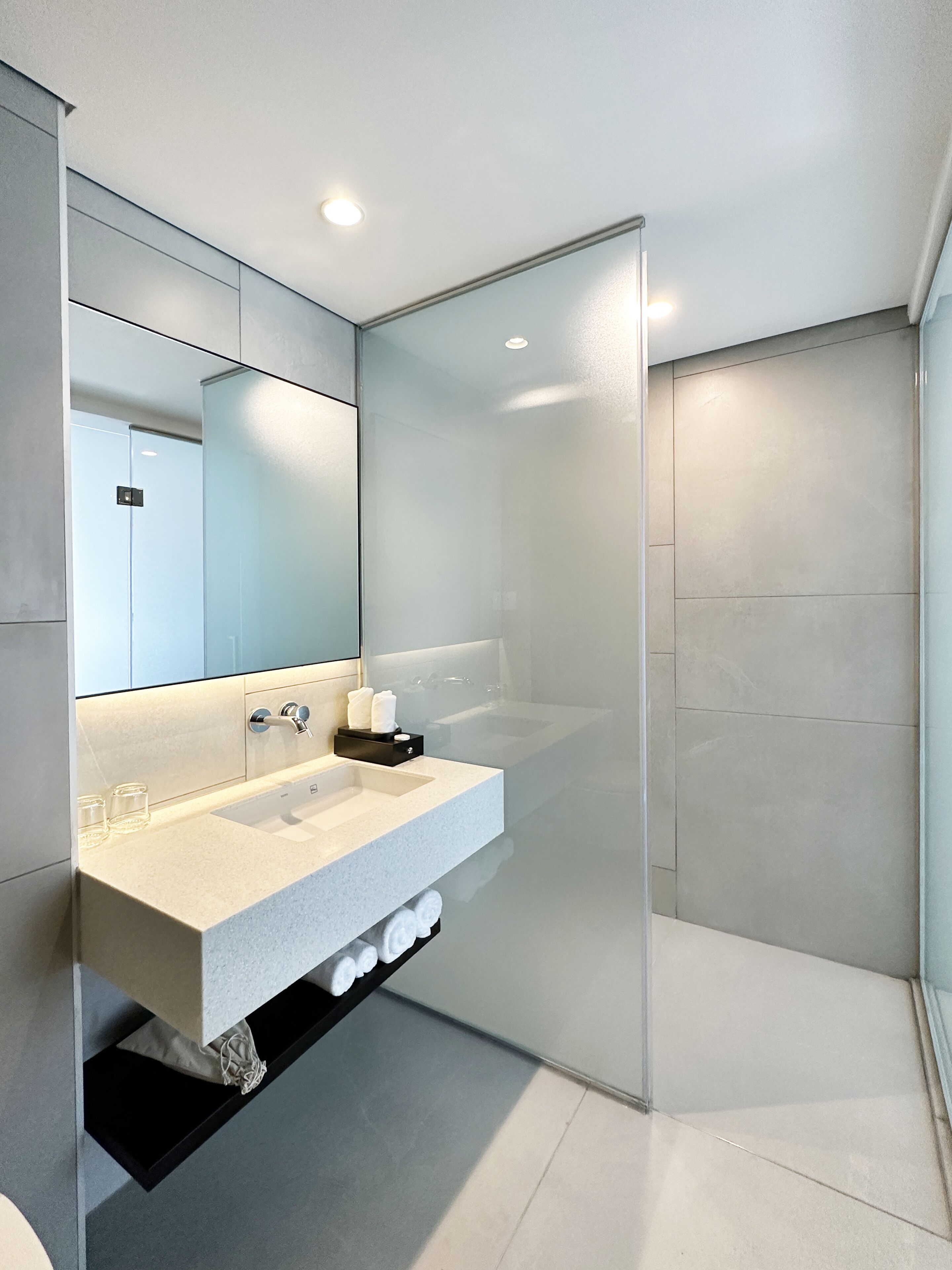 Un baño moderno con cabina de ducha de vidrio, un lavabo blanco y un plato para jabón negro, y un espejo sobre el lavabo.