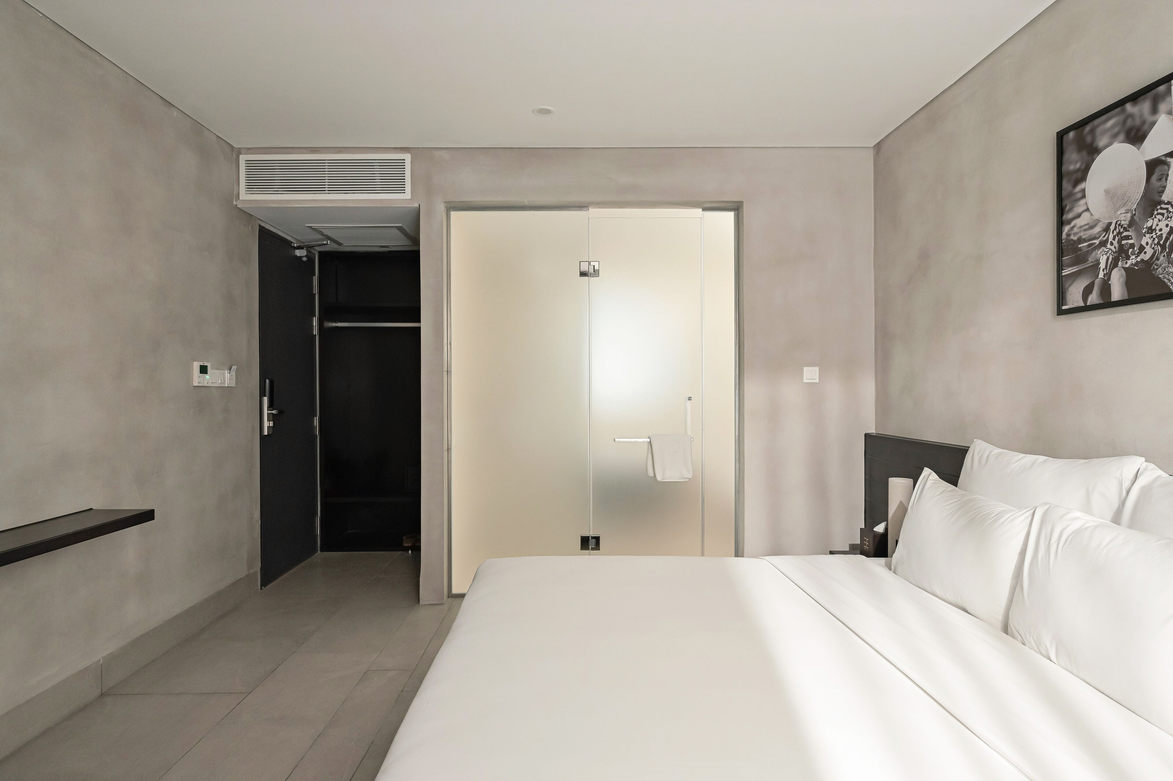 Una habitación de hotel moderna con una cama grande, un armario y un baño visible a través de una puerta abierta.