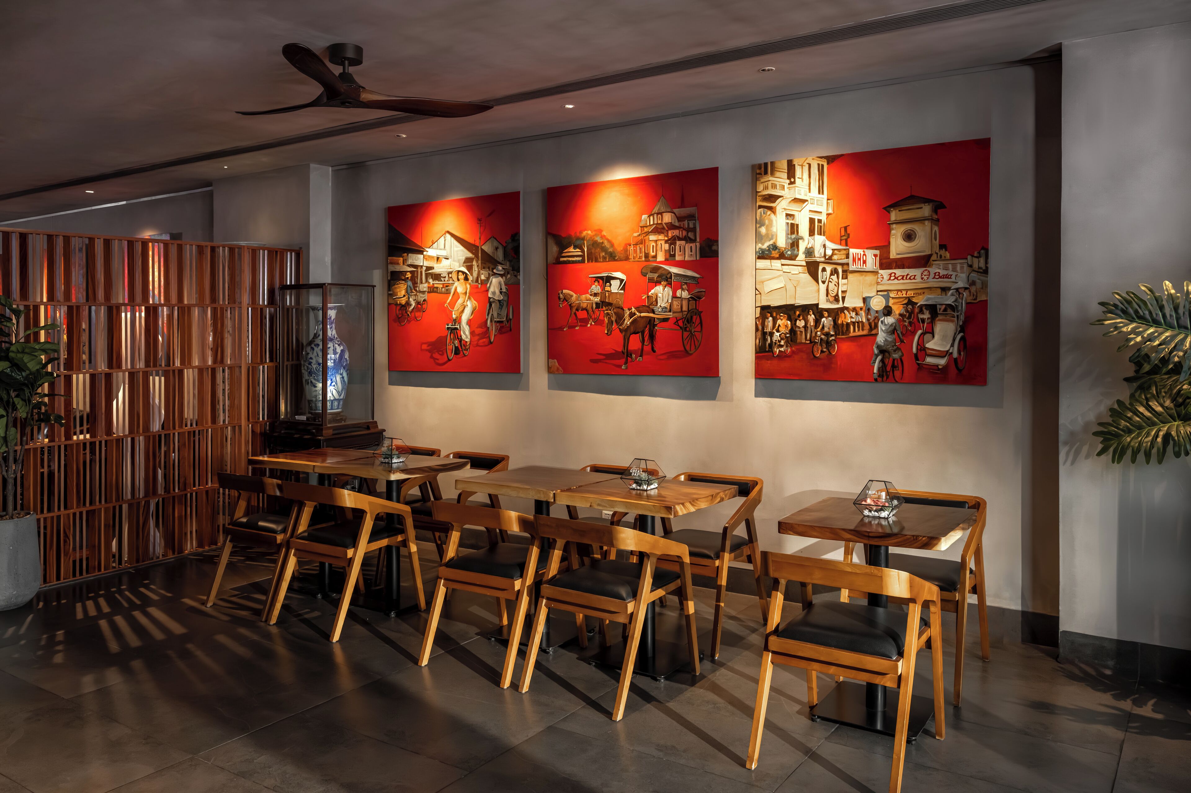 Interior de restaurante com mesas e cadeiras de madeira, um painel decorativo de madeira e três grandes murais vermelhos retratando cenas históricas.