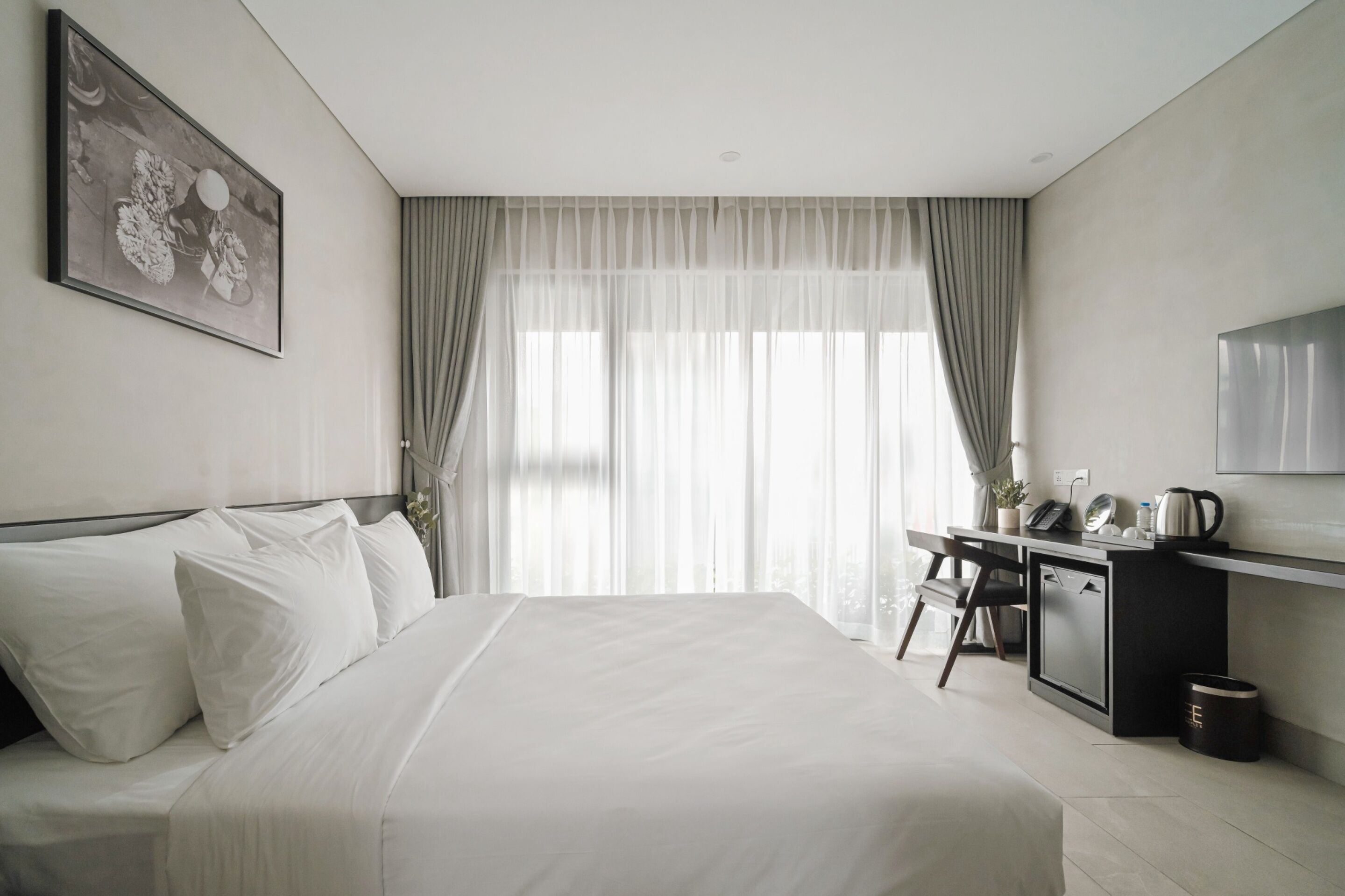 A modern hotel room with a large bed, a desk with a kettle, and a TV on the wall.