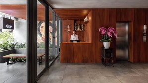 Un área de recepción con un mostrador de madera, una orquídea en maceta grande y un letrero en la pared.