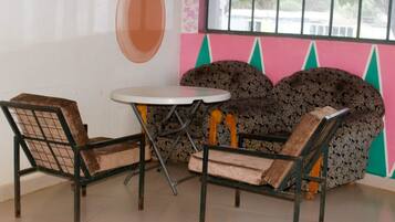 Una habitación con dos sillas y una mesa pequeña, una ventana con rejas y una pared de colores con diseños geométricos.