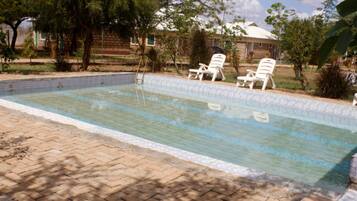 Una piscina con borde de azulejos, rodeada por un patio de ladrillo y dos sillones blancos.