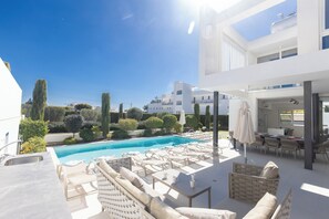 A modern outdoor pool area with lounge chairs, a dining area, and a view of the surrounding landscape. - Ayia Napa Kube Villa Kb2 (Ayia Napa)