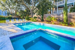 A rectangular swimming pool with a tiled edge, surrounded by a wooden fence, and shaded by trees.