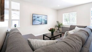 Ein Wohnzimmer mit grauem Sofa, einem schwarzen Couchtisch, einer Topfpflanze und einem gerahmten Bild an der Wand.