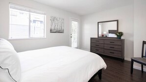 Ein Schlafzimmer mit einem großen Bett, einem Schminktisch, einem Spiegel und einem Fenster mit Jalousien.