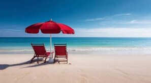 A beach with two red chairs and a red umbrella. - The Salty Stay |WOW!! 1PM Check in! | FREE Golf Cart & Beach Chairs Included | Super Cute Location! Near Ice Cream & Coffee! (Miramar Beach)
