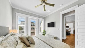 Een slaapkamer met een groot bed, een plafondventilator, een aan de muur bevestigde televisie en uitzicht op het balkon.