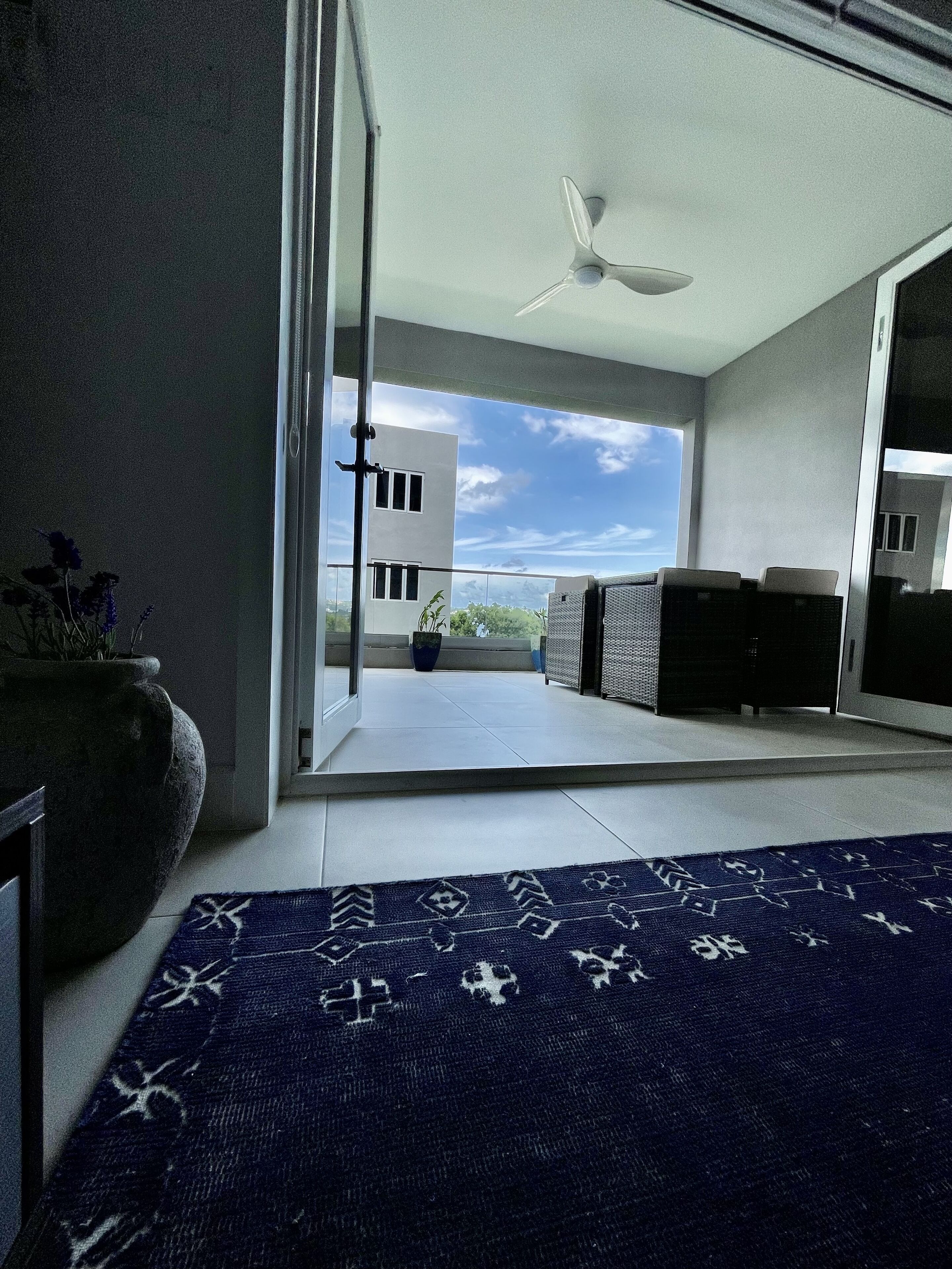 Een moderne kamer met een grote schuifdeur die leidt naar een balkon met uitzicht op een gebouw en een heldere lucht.