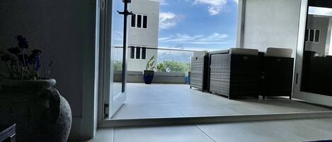 Een moderne kamer met een grote schuifdeur die leidt naar een balkon met uitzicht op een gebouw en een heldere lucht.