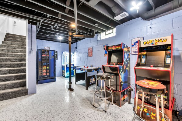 A retro arcade with classic games like Pac-Man and Mortal Kombat, a foosball table, and a staircase leading to another level.