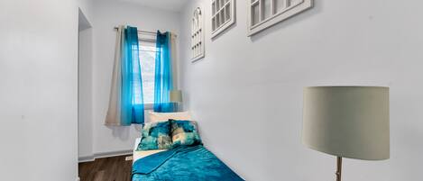 Un dormitorio con cama, lámpara y ventana con cortinas.