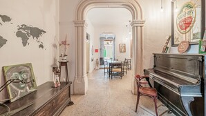 A room with a piano, a world map on the wall, and a dining area in the background. - Holiday Home "Townhouse Can Miquel" with Pool, Garden and Wi-Fi (Sa Pobla)