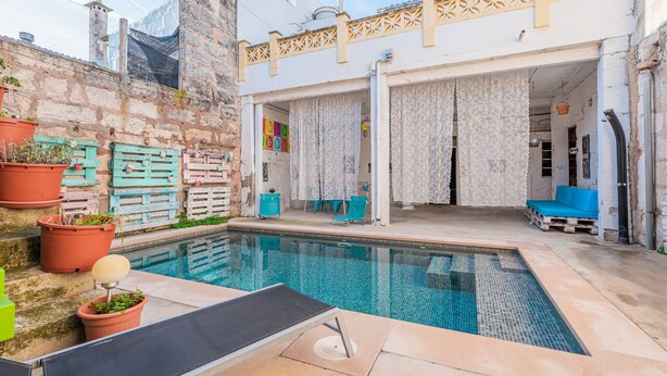 A swimming pool with a sun lounger, a covered patio area, and a stone wall with potted plants. - Holiday Home "Townhouse Can Miquel" with Pool, Garden and Wi-Fi (Sa Pobla)