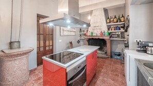 A kitchen with a central island, a built-in oven, a hanging pot rack, and a brick fireplace. - Holiday Home "Townhouse Can Miquel" with Pool, Garden and Wi-Fi (Sa Pobla)
