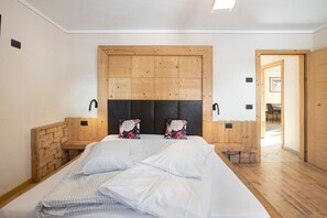 A bedroom with a wooden headboard, a bed with white linens, two bedside tables with lamps, and a wooden bench at the foot of the bed. - "Appartamento 1 Deluxe - Alpen Suite" with Mountain View, Garden & Wi-Fi (Livigno)