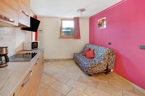 Una cocina compacta con microondas, estufa y una ventana pequeña con cortinas.