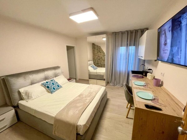 A hotel room with a bed, a desk with a chair, a television, and a bathroom visible through a glass door. - Channel Suite - 3 (Sinalunga)