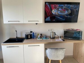 Cocina compacta con lavamanos, tostadora, tetera, microondas y un televisor de pantalla plana montado en la pared.