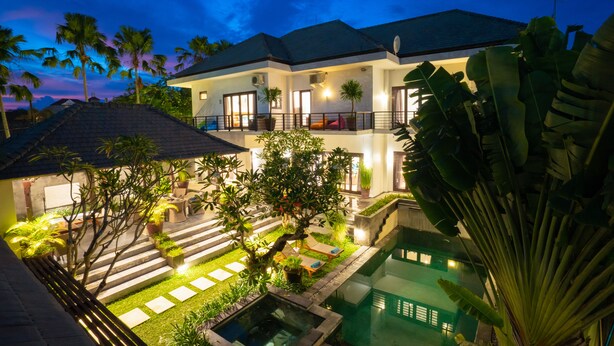 Una casa de dos pisos con piscina, rodeada de palmeras y espacios exteriores bien iluminados.