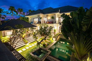 A two-story house with a swimming pool, surrounded by palm trees and well-lit outdoor areas. - Echo Suji Villa (Canggu)