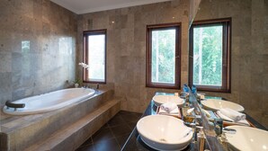 Un baño moderno con una bañera grande, dos lavamanos y un tocador con espejo.