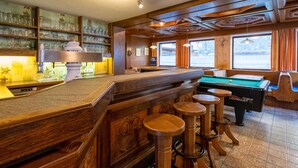Zona de bar con mesa de billar, taburetes y barra con cristalería.