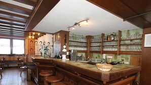 Zona de bar con taburetes de madera, una barra y estantes con vasos y botellas.