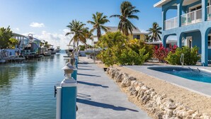 A marina with boats docked, a swimming pool, and a building with a blue facade. - Sandal Escape: 6BR Canal Front Oasis w/ Heated Pool, Dog-Friendly, Dockage & Fast Atlantic Access (Marathon)