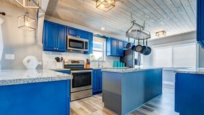 A modern kitchen with blue cabinets, stainless steel appliances, and a central island. - Sandal Escape: 6BR Canal Front Oasis w/ Heated Pool, Dog-Friendly, Dockage & Fast Atlantic Access (Marathon)