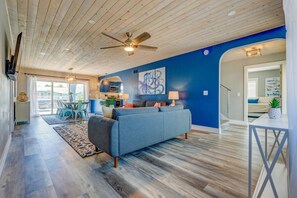 A spacious living room with a blue sofa, wooden flooring, and a ceiling fan.