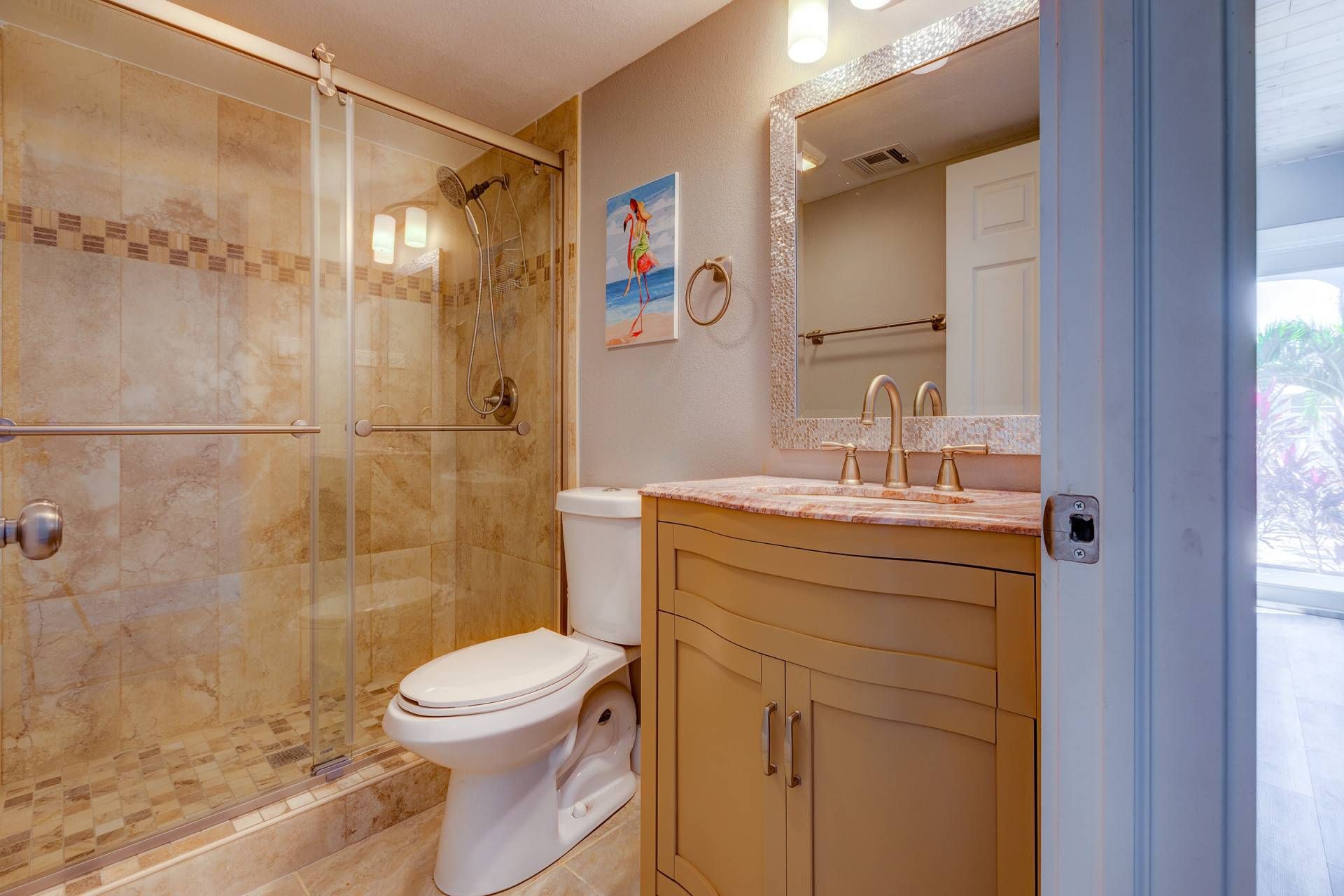 A bathroom with a glass-enclosed shower, a toilet, a sink with a mirror, and a view of the outdoors.
