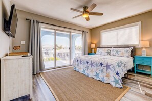 A bedroom with a large sliding glass door leading to a balcony, a ceiling fan, a bed with star-patterned bedding, and a nightstand with a lamp.
