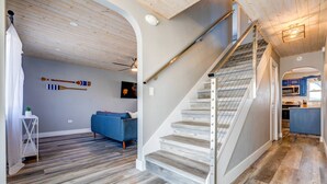 A modern interior with a wooden staircase, a blue sofa, and a kitchen area. - Sandal Escape: 6BR Canal Front Oasis w/ Heated Pool, Dog-Friendly, Dockage & Fast Atlantic Access (Marathon)