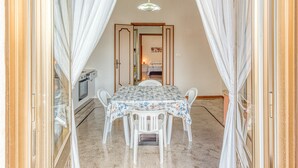 Un comedor con una mesa preparada para cuatro, sillas blancas, mantel estampado y una araña.