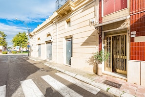 A street view with a building featuring a gated entrance, a potted plant, and a clear sky.