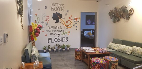 A living room with a sofa, coffee table, and decorative items. There is a wall with a quote and a silhouette of a woman. - Hotel Fleur (Jaipur)