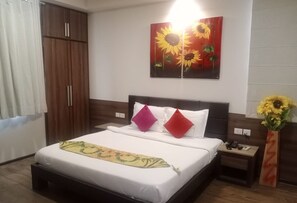 A hotel room with a bed, a nightstand, a vase with sunflowers, and a large painting of sunflowers on the wall. - Hotel Fleur (Jaipur)