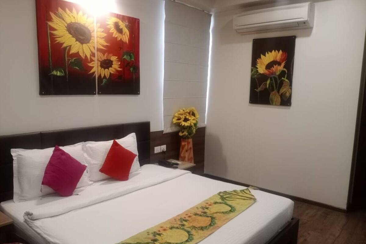 A hotel room with a bed, a nightstand, a vase with sunflowers, and two paintings of sunflowers on the walls.
