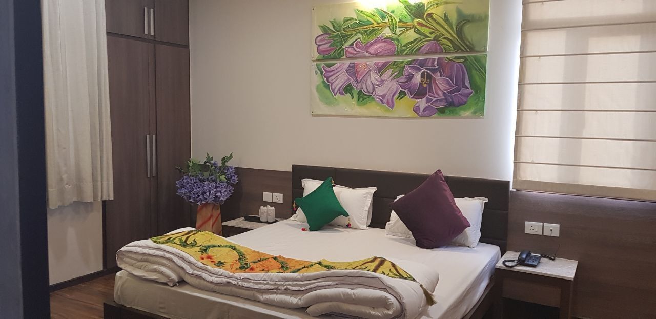 A hotel room with a bed, a nightstand, a telephone, a vase with flowers, and a painting on the wall.