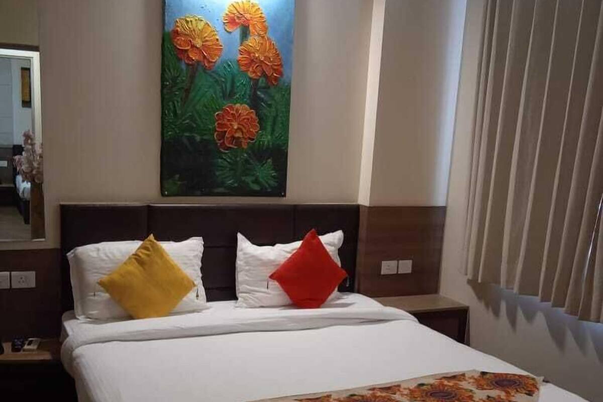 A hotel room with a large bed, a painting of flowers on the wall, and a window with curtains.