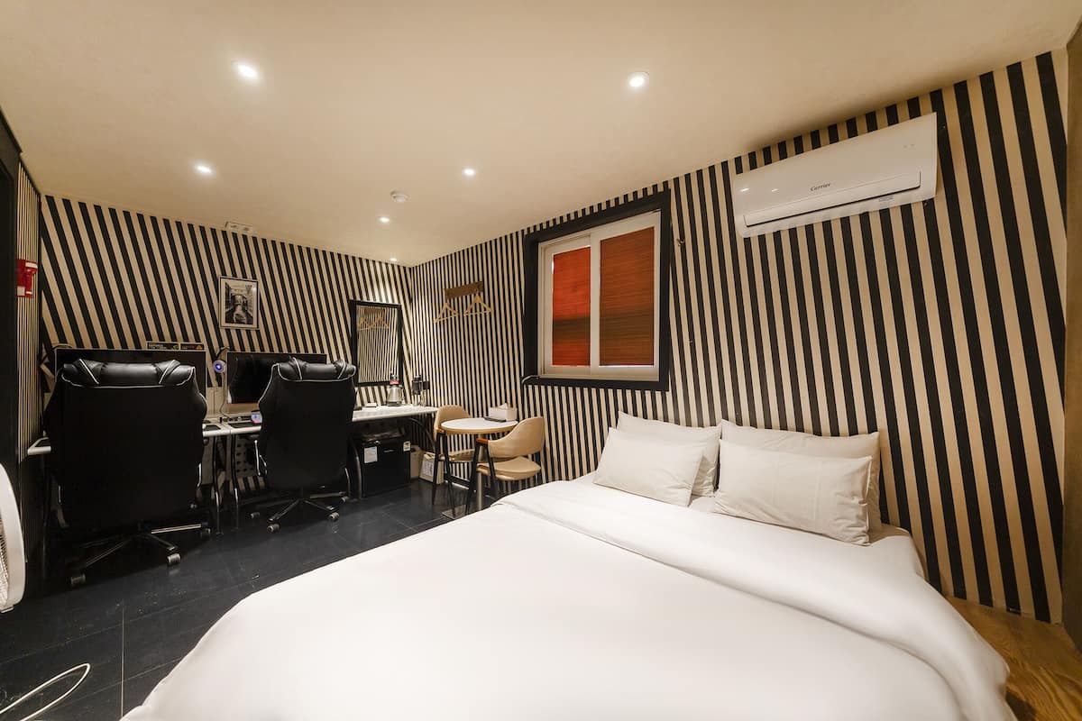 A hotel room with a bed, a desk with two chairs, an air conditioner, and striped wallpaper.