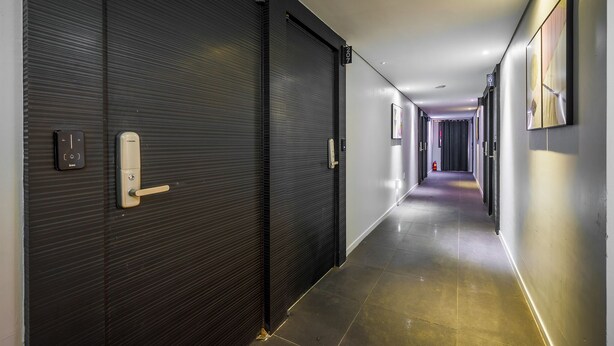 Un pasillo con puertas cerradas, un extintor y un cartel que indica la habitación número 207.
