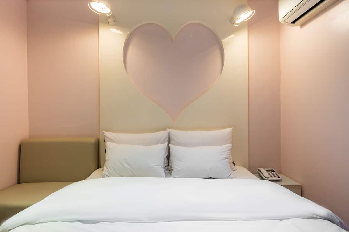 A hotel room with a bed, a bedside table with a phone, and a heart-shaped light fixture on the wall.