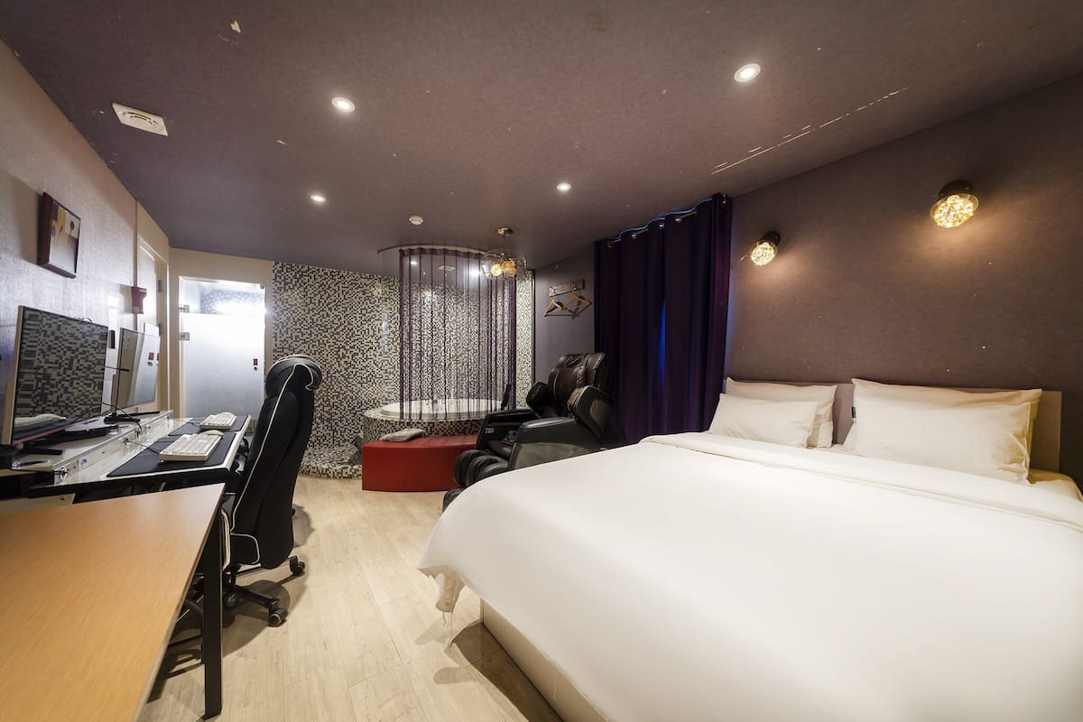 A hotel room with a bed, desk, computer, and a shower area.