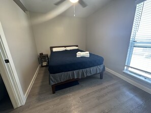 Cozy retreat with a neatly made bed, nightstand, and large window with blinds.