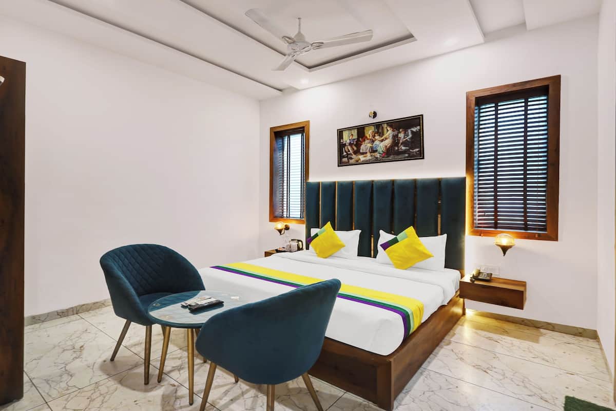 A bedroom with a bed, two chairs, a ceiling fan, and a painting on the wall.
