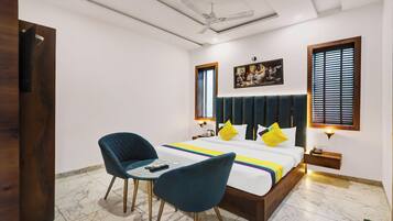 A bedroom with a bed, two chairs, a ceiling fan, and a painting on the wall.